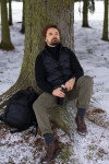 Mand i hue og vest laener sig op ad trae i snevejr
