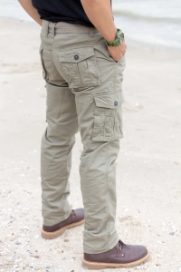 Person i overlevelses cargo bukser staar med haenderne i lommen paa sandstrand