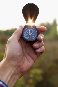 Haand der holder feltkompas med lys aabent, omgivet af natur og solnedgang